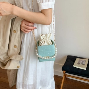 Light green drawstring bucket bag with pearl handle and gold chain strap shown on model