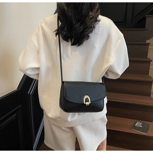 Detail of minimalist black leather crossbody bag with gold U-shaped buckle on a model