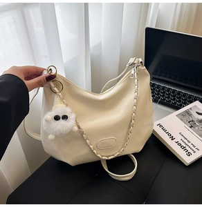 Detail of beige half-moon shoulder bag with chain strap and plush doll charm