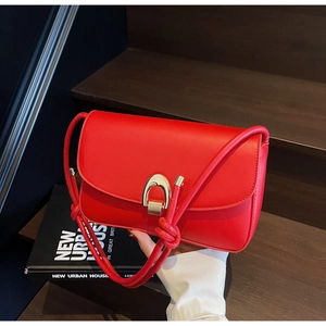 Detailed close-up of a red leather square bag with golden horseshoe buckle on wooden stairs