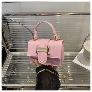 Pink crossbody bag held by hand featuring a gold clasp and elegant chain strap detail