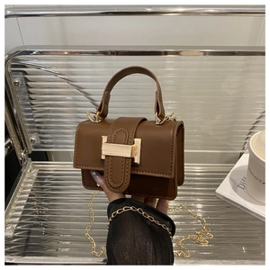 Detail of a brown leather crossbody bag with a gold metal clasp and chain strap