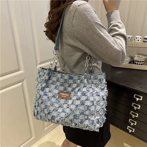 Blue denim checkered tote bag with fringe detail and chain strap shown on model
