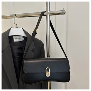 Detail of minimalist black leather shoulder bag featuring a gold oval twist-lock closure