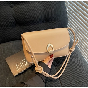 Detail of cream leather shoulder bag featuring a gold horseshoe buckle and rope strap