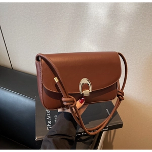 Detail of caramel brown leather shoulder bag with gold horseshoe buckle and knotted strap