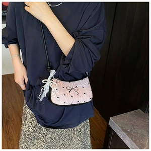 Detail of pink pleated crossbody bag with black bow print and pearl lace charm accessory