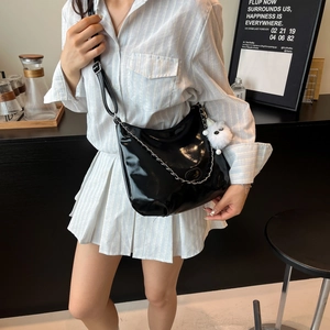 Glossy black crescent crossbody bag with silver chain and plush charm on female model