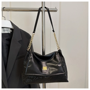 Detail of black faux leather handbag with snake pattern texture and gold chain strap