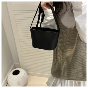 Detailed shot of a black leather bucket bag worn cross-body with adjustable shoulder strap