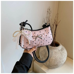 Detail of pink pleated handbag with heart print, pearl lace bow, and metal bow charm