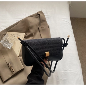 Détail du sac à paillettes noir avec boucle dorée sur literie blanche et blazer