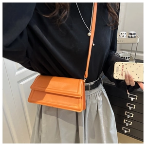 Detail of bright orange square crossbody bag featuring refined stitching and adjustable strap