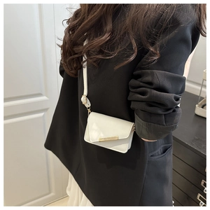 Close-up of a white mini flap bag with gold hardware and adjustable strap on a black blazer