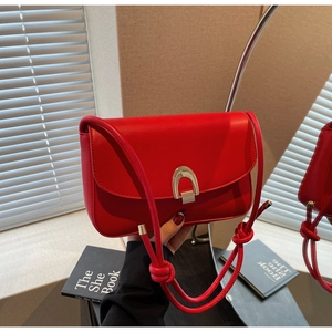 Detail of red square bag with golden horseshoe clasp and knotted leather shoulder strap