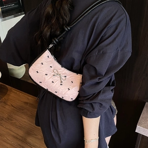 Pink underarm bag with black bow prints and silver metallic buckle shown on shoulder