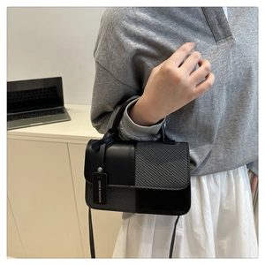 Dettaglio della borsa a tracolla nera con texture miste ed etichetta moda sul manico