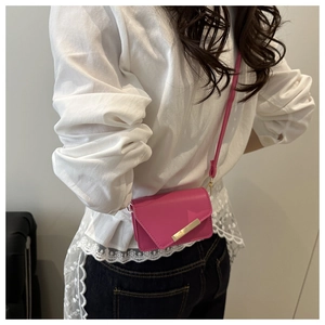 Detail of fuchsia leather mini crossbody bag with gold metal buckle on casual outfit