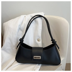 Detail of black matte leather baguette bag with knotted straps and gold buckle on a white chair