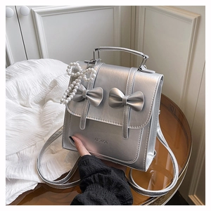 Detail of silver metallic backpack with bow accents and pearl charm on a glass table