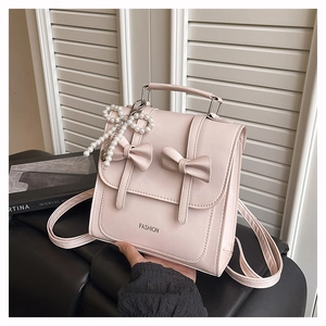 Detail of light pink backpack featuring 3D bows and pearl charm in a cozy setting