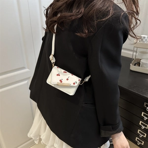 Fashionable white crossbody bag with red cherry print and gold hardware worn by model
