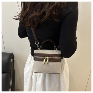 Detail of canvas and brown leather mini box bag with golden zippers worn by a model