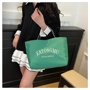 Detail of green nylon tote bag featuring side pockets and striped woven shoulder strap