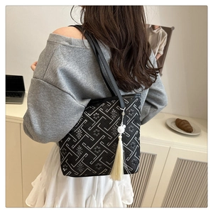 Detail of embroidered tote bag with geometric pattern and white tassel charm on model