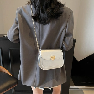 Silberne Damen-Umhängetasche aus Lackleder mit goldenem Herzverschluss am Modell