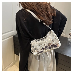 Detail of silver sequin shoulder bag with chain strap worn by a model in a modern home