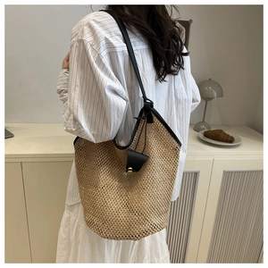 Close-up of woven straw tote bag with black leather straps on a female model