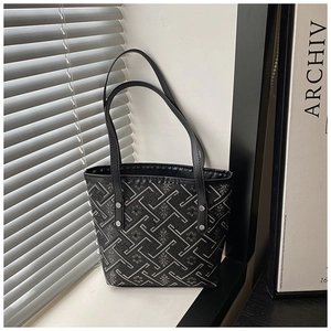 Detail of black tote bag featuring geometric fretwork embroidery and leather edge piping