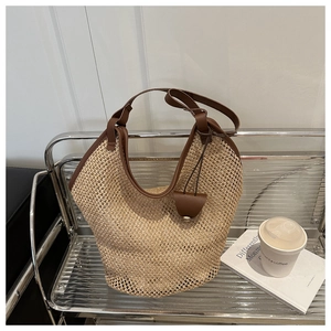 Close-up of beige woven straw tote bag featuring brown leather trim and texture details