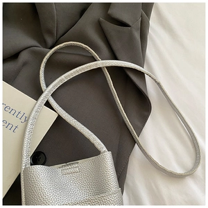 Detailed close-up of a silver pebbled leather mini crossbody bag on a textured grey blazer