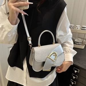 Silver metallic saddle bag with gold D-buckle shown on model in a minimalist setting