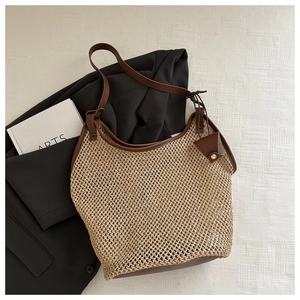 Dettaglio della borsa tote in paglia intrecciata con manici in pelle marrone su un blazer