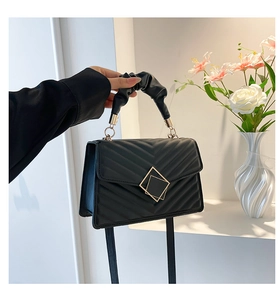 Detail of V-quilted black handbag featuring a scrunchie handle and golden lock clasp