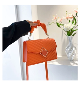 Detail of orange quilted handbag with twisted handle and square metal buckle ornament