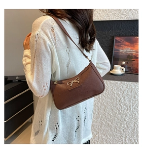Close-up of caramel brown pebble texture faux leather bag with golden bow hardware detail