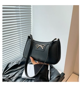 Detail of black pebbled leather half-moon bag featuring a gold bow metallic buckle