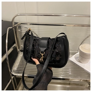 Close-up of black sequin baguette bag with golden metal clasp on a stylish shelf