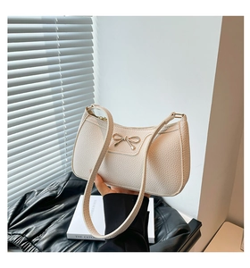 Close-up of white lychee pattern leather baguette bag with a gold bow buckle detail