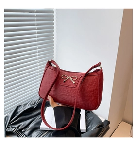 Close-up of red lychee grain leather handbag featuring a gold metal bow decoration