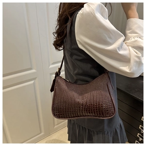 Detail of dark brown crocodile embossed shoulder bag on model with gold hardware