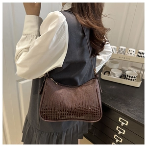 Detail shot of a dark brown crocodile texture shoulder bag worn with casual stylish outfit