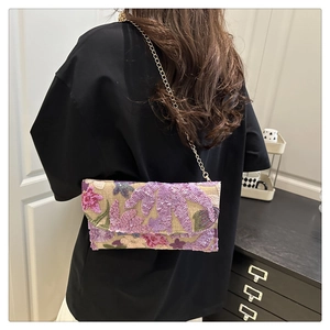 Detail van de bloemige lovertjes borduursels en gouden ketting op de geweven tas