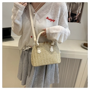 Detalle de bolso de paja tipo concha beige con asas de PU blanco y detalles en metal dorado