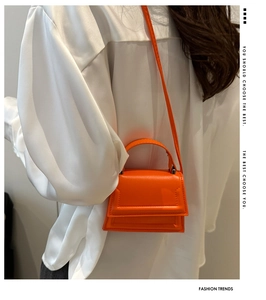 Detail of bright orange micro leather bag worn by model with a white satin shirt