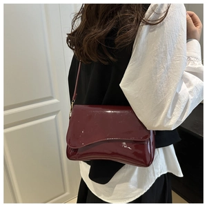 Close-up of glossy burgundy patent leather shoulder bag with gold hardware detail